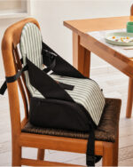 Silla booster a rayas verde colocada en una silla de madera junto a la mesa